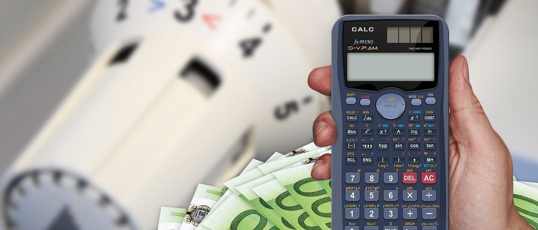 Hand hält einen Taschenrechner über Geldscheine, mit einer Uhr im Hintergrund, die 3:00 Uhr anzeigt.