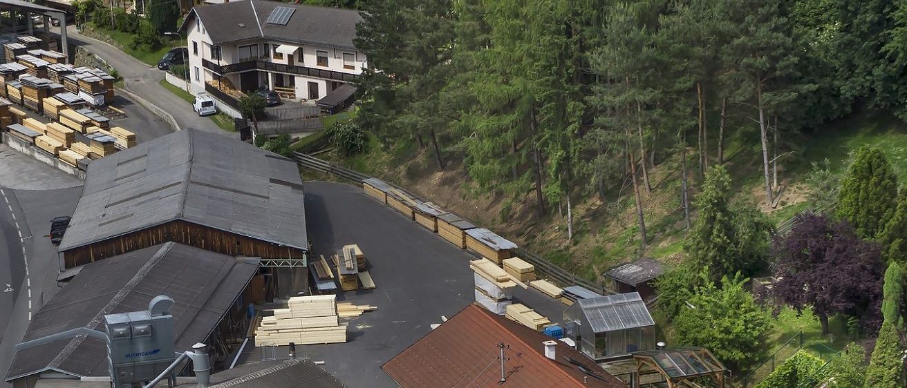 Luftaufnahme eines Wohngebiets mit Häusern, einer Auffahrt und einem Holzstapel auf der Straße. Die Häuser haben Solarpanels, und es gibt Bäume am Hang.
