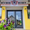 Die Ladenfront von Bucher Buben KG mit einem Schild über dem Eingang. Der Laden bietet Bücher und Spielzeug an und modellt Züge. Eine Lampe beleuchtet den Eingang, und eine Blumenpflanze steht davor.