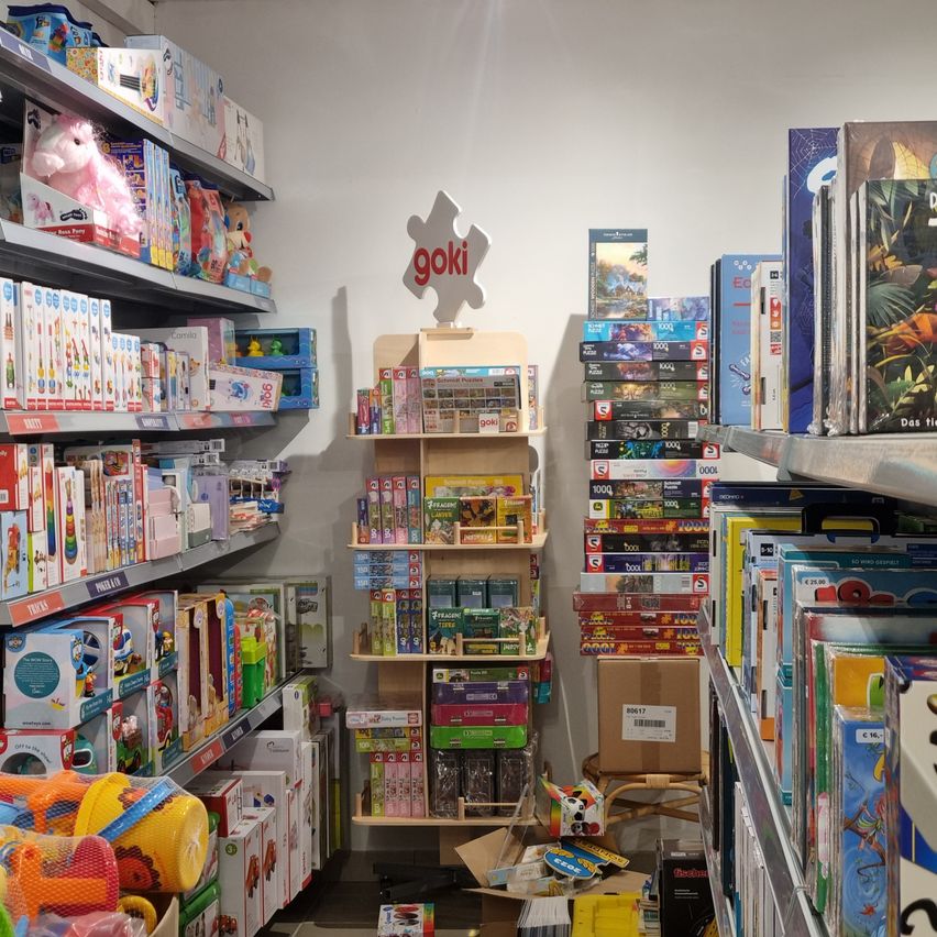 A toy store with various toys on shelves. A sign with the word goki is on the wall. Some toys are on the floor.
