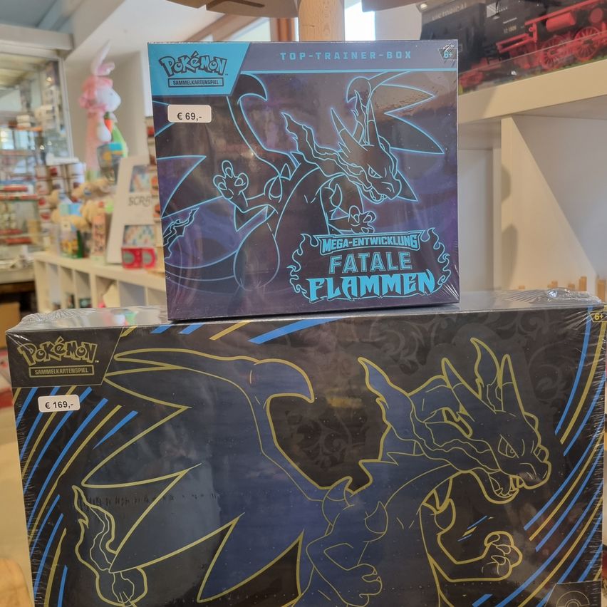 Two Pokemon boxes are displayed in a store. The top box is blue and features a dragon design. The bottom box is black with a dragon design. Both boxes are unopened.