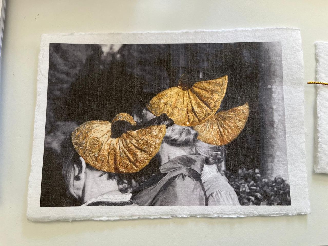 A black and white photograph of three women wearing golden hats with intricate designs. The hats are prominently displayed, and the background is blurred.