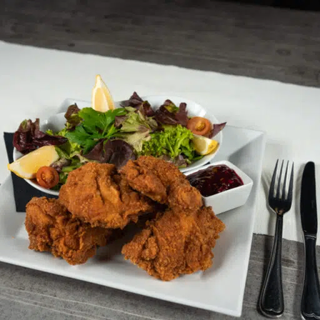 Ein weißer Teller mit frittiertem Hähnchen und einem Salat mit Zitronenscheiben auf einem Tisch.