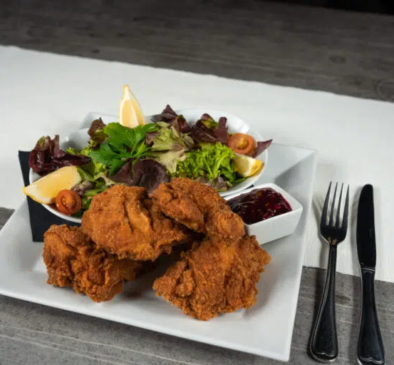 Ein weißer Teller mit frittiertem Hähnchen und einem Salat mit Zitronenscheiben auf einem Tisch.