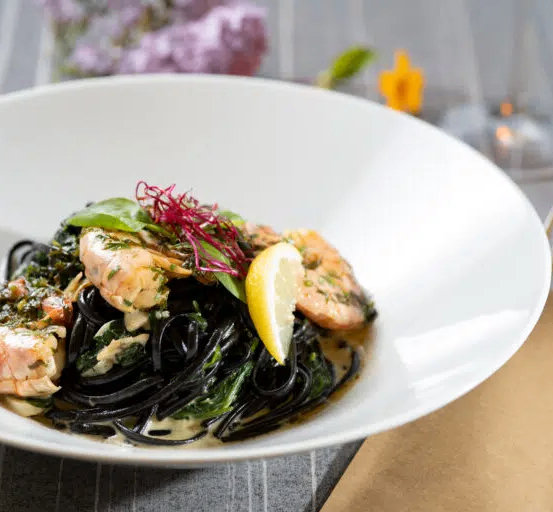 Ein weißer Teller mit einem Gericht aus schwarzen Nudeln, Garnelen und Garnierung.