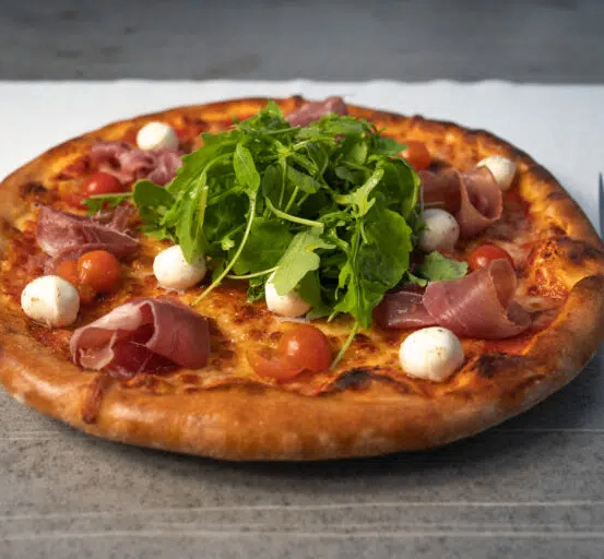 Eine frisch gebackene Pizza mit goldener Kruste, belegt mit Mozzarella, Kirschtomaten, Prosciutto und Rucola.