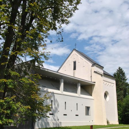 Ein modernes Gebäude mit weißer Fassade und geometrischen Mustern. Das Gebäude ist von üppigem grünen Bäumen und Gras umgeben.