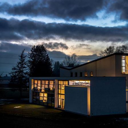 Ein modernes Gebäude ist bei Dämmerung beleuchtet, mit klarem Himmel darüber und einem geparkten Auto davor.