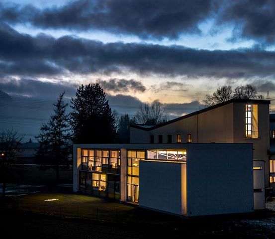 Ein modernes Gebäude ist bei Dämmerung beleuchtet, mit klarem Himmel darüber und einem geparkten Auto davor.