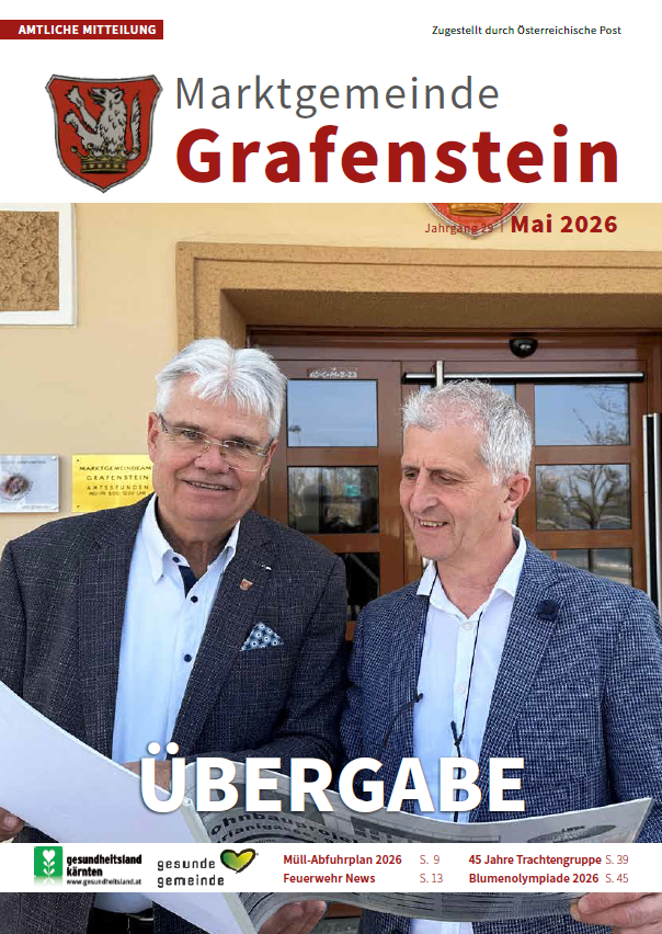 Zwei Männer stehen vor einem Gebäude mit einem Schild, das 'Übergabe' sagt. Der Mann auf der linken Seite hält ein Stück Papier. Der Mann auf der rechten Seite trägt eine blaue Jacke mit einem weißen Innenshirt.