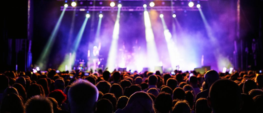 Eine große Menschenmenge bei einem Konzert mit hellen Bühnenlichtern, die die Künstler auf der Bühne beleuchten.