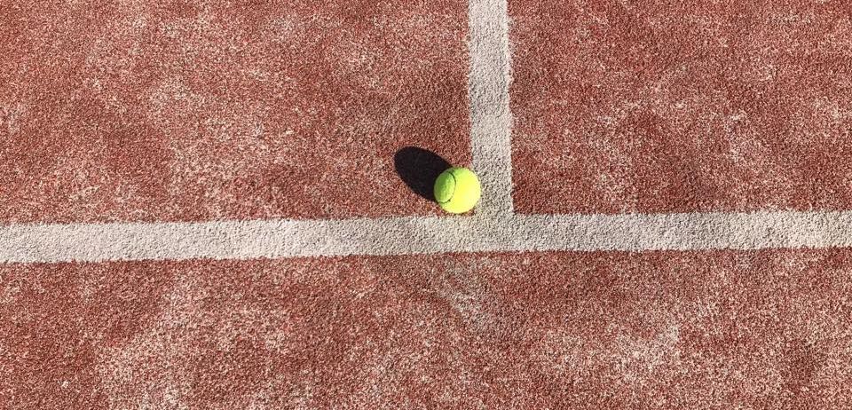 Ein Tennisplatz mit einem gelben Tennisball, der in der Nähe der weißen Linie auf dem Boden platziert ist.