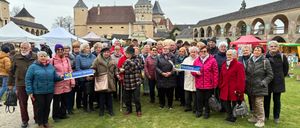 Eine Gruppe von Menschen in Winterkleidung versammelt sich auf einem Grasfeld und hält Banner mit dem Wort 'NEIN'. Dahinter steht ein Gebäude mit einem Turm.