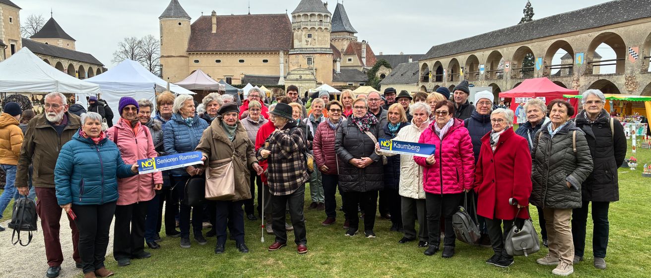 Eine Gruppe von Menschen in Winterkleidung versammelt sich auf einem Grasfeld und hält Banner mit dem Wort 'NEIN'. Dahinter steht ein Gebäude mit einem Turm.