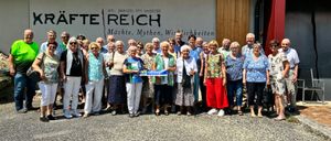 Eine Gruppe von Menschen steht vor einem Gebäude mit 'St. Jakob im Walde' und 'Fete Reich' darauf geschrieben. Sie tragen Freizeitkleidung und einige halten ein Schild mit 'NEIN' und 'Kaumberg.'