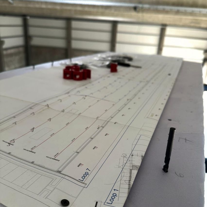 A blueprint on a table includes 'Loop 1' and 'Loop 7' markings, along with various tools and fasteners.