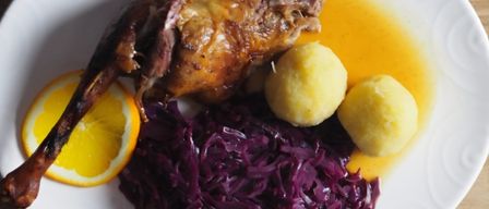 Ein weißer Teller mit gebratener Ente, Kartoffelpüree und Rotkohl. Eine Orangenscheibe ist links.