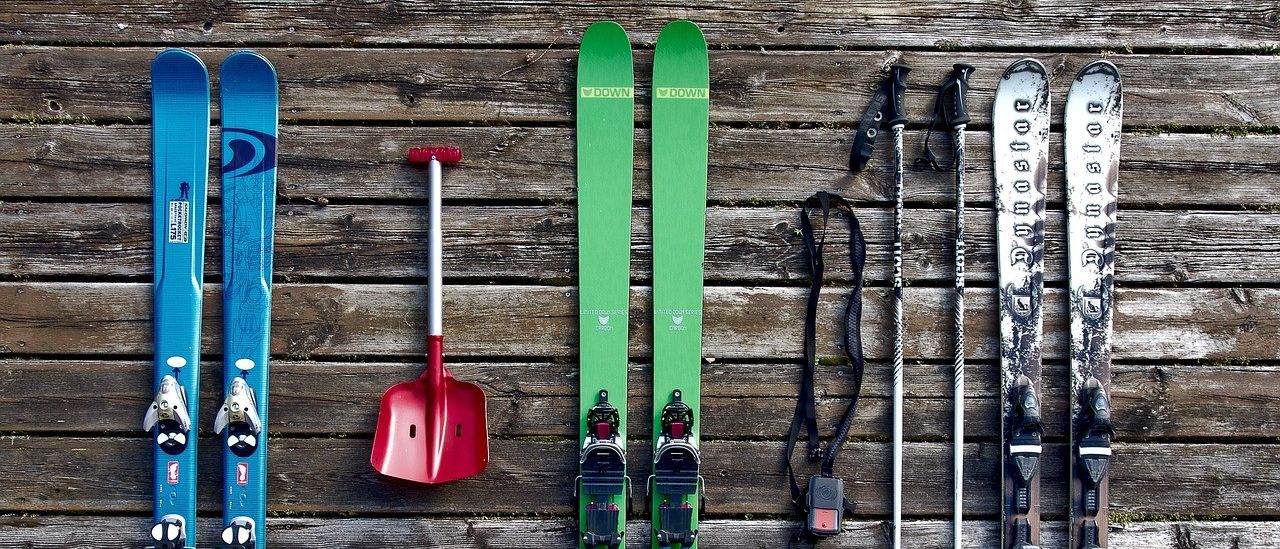Eine Auswahl an Skiausrüstung, darunter ein Paar Skier, Skischuhe und Skistäbe, auf einer Holzoberfläche ausgestellt.