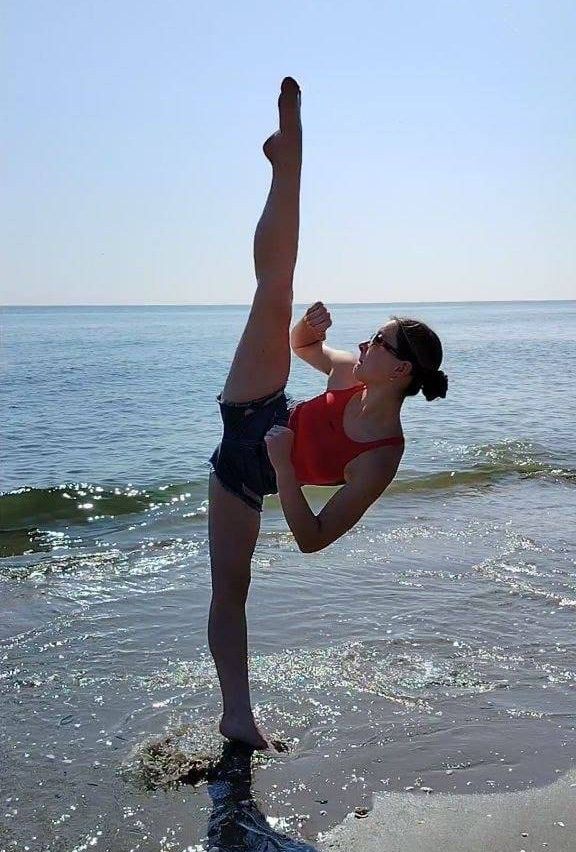 Eine Frau führt einen Handstand am Strand mit dem Ozean im Hintergrund aus.