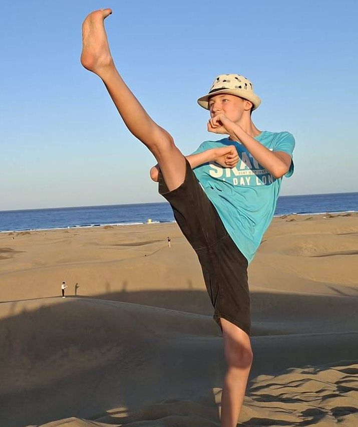 Ein junger Junge führt eine Kampfkunstpose auf einem sandigen Strand mit dem Ozean im Hintergrund aus.