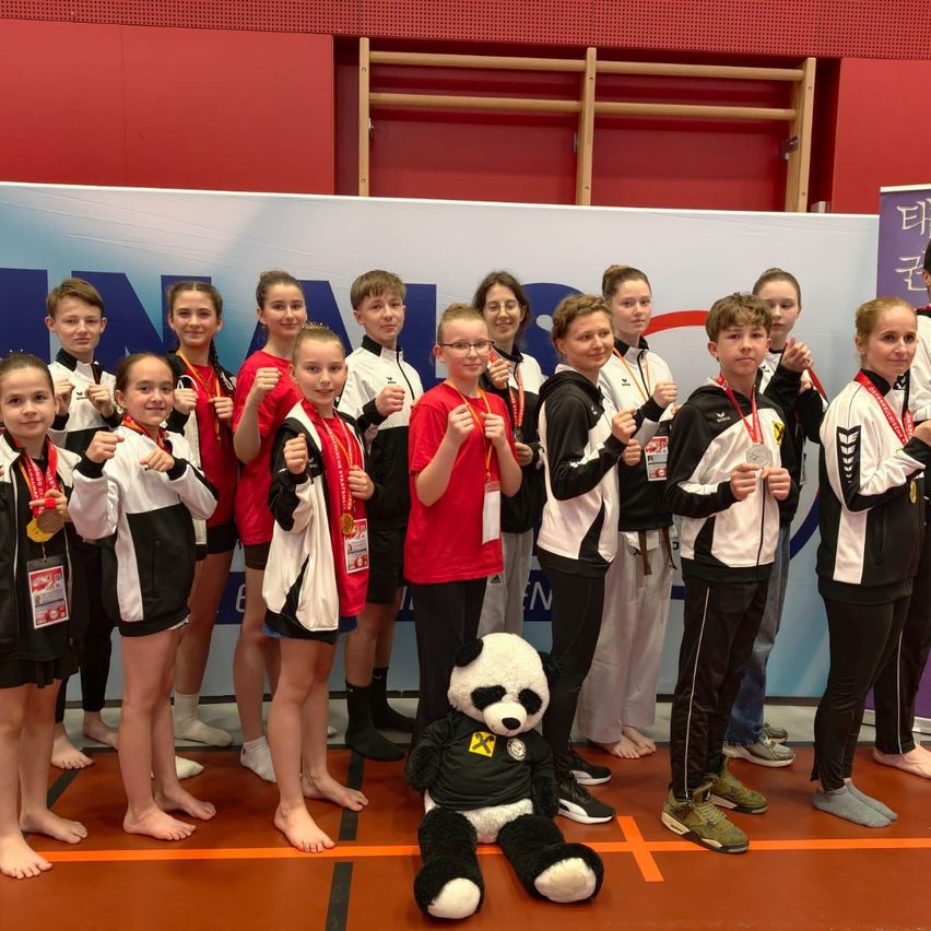 Eine Gruppe von Kindern und Jugendlichen posiert für ein Foto mit Medaillen um den Hals und steht in einer Turnhalle mit einem Panda-Maskottchen auf dem Boden.
