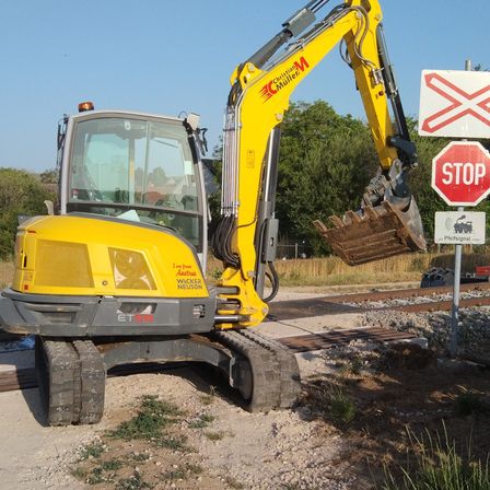 Ein gelber Baufahrzeug steht auf einer Eisenbahnschiene. Der Bagger hat eine Schaufel und ein Schild mit einem roten Stoppschild in der Nähe.