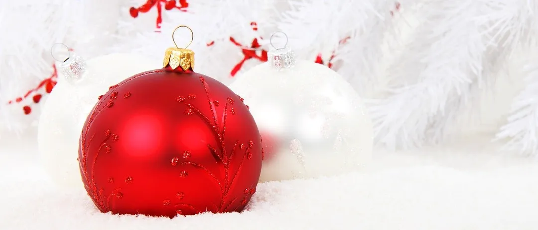 Zwei Weihnachtskugeln, eine rote mit dekorativen Mustern und eine weiße mit Schneeflockendesigns, liegen auf einer Schneebettdecke mit einem weißen Tinsel-Hintergrund.