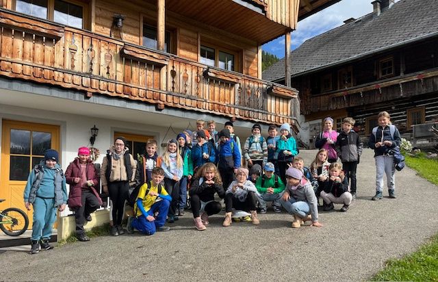 Eine Gruppe von Kindern und Erwachsenen posiert für ein Foto vor einem Holzhaus an einem bewölkten Tag.