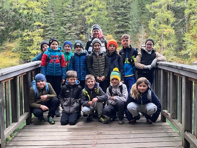 Eine Gruppe von Kindern und Erwachsenen posiert für ein Foto auf einer Holzbrücke in einem bewaldeten Gebiet.