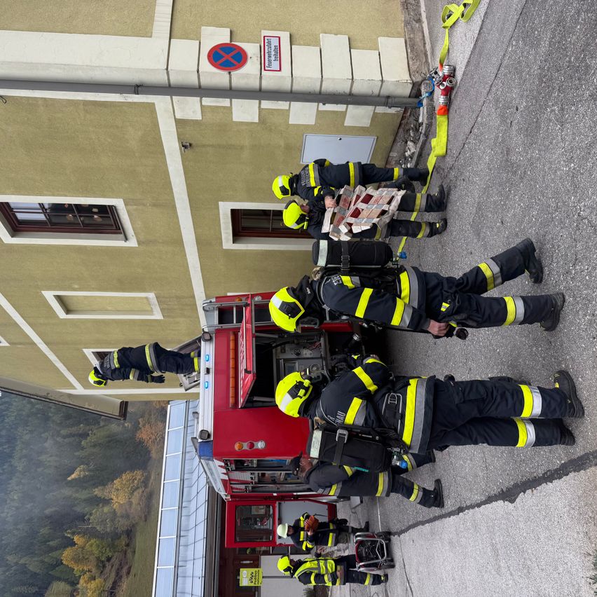 Feuerwehrleute in gelben und schwarzen Uniformen stehen auf der Straße und kümmern sich um einen Feuerwehrwagen. Das Gebäude hat ein Schild, das 'verboten' besagt.