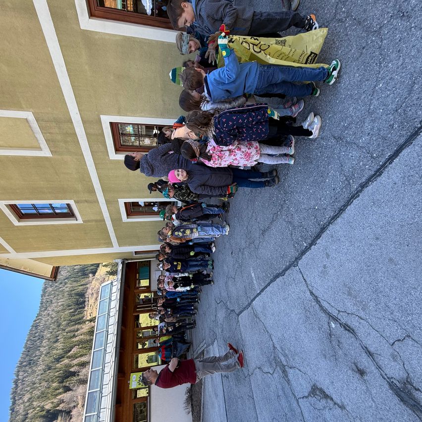 Eine Gruppe von Kindern und Erwachsenen steht in einer Reihe vor einem Gebäude, einige mit Handschuhen. Ein Mann in einem roten Shirt steht am Ende.