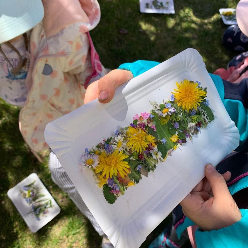 Eine Person hält einen Pappteller mit verschiedenen Blumen darauf, möglicherweise an einer naturthematischen Aktivität teilnehmend.
