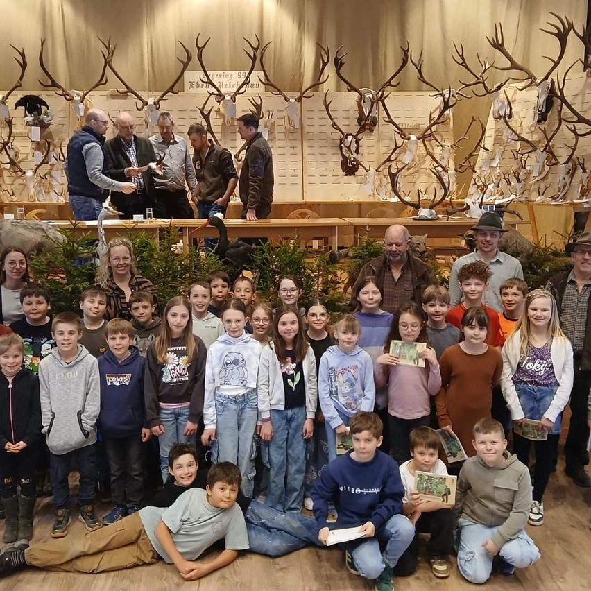 Eine Gruppe von Kindern und Erwachsenen posiert für ein Foto in einem Raum mit Hirschgeweihen an der Wand. Die Kinder halten Zertifikate in den Händen.