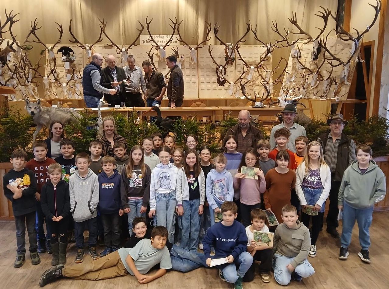 Eine Gruppe von Kindern und Erwachsenen posiert für ein Foto in einem Raum mit Hirschgeweihen an der Wand. Die Kinder halten Zertifikate in den Händen.