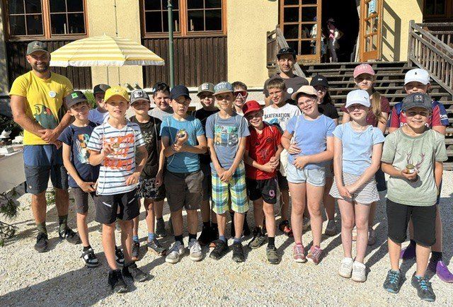 Eine Gruppe von Kindern und zwei Männern posiert für ein Foto vor einem Gebäude, einige halten Medaillen.