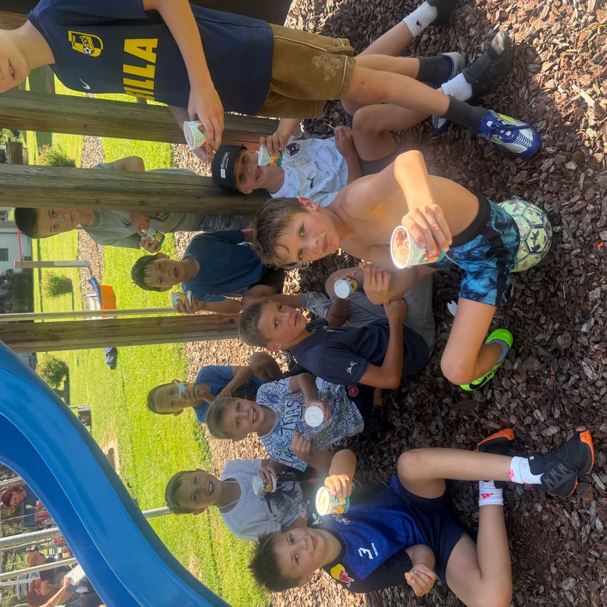 Eine Gruppe von Jungen sitzt auf dem Boden und isst Eis in einem Spielplatz.