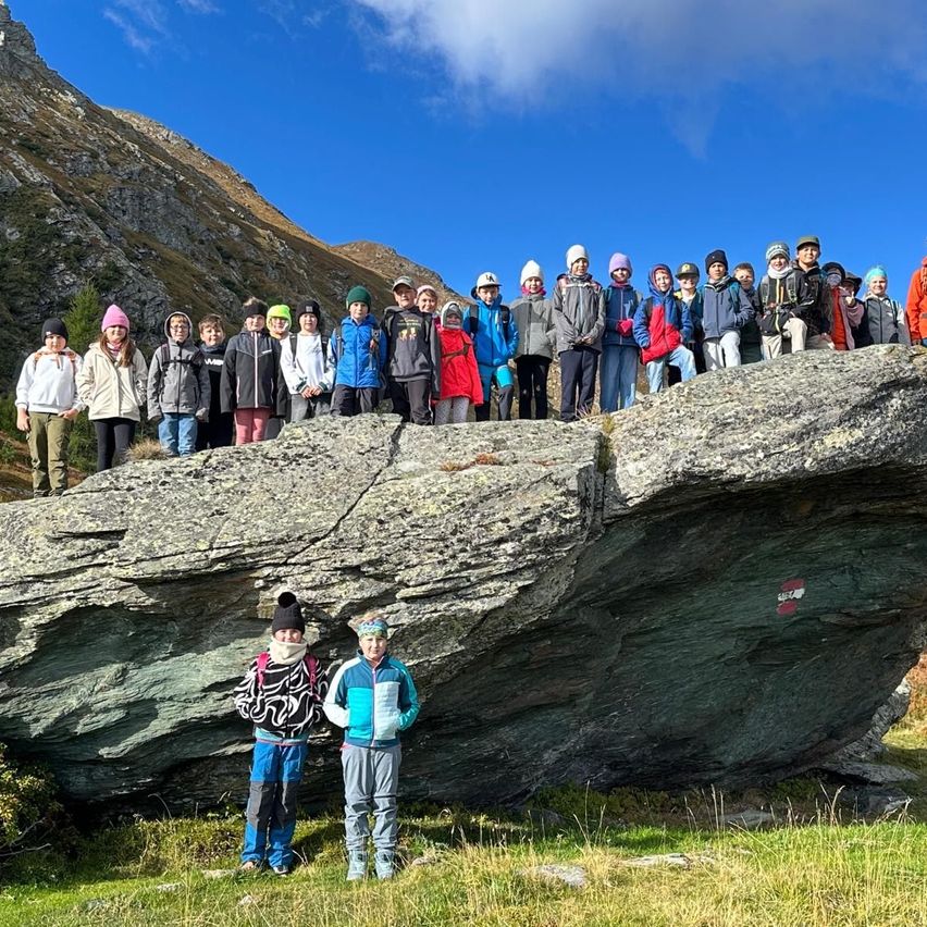 Eine Gruppe von Kindern und Erwachsenen steht auf einem großen Felsen in einem Gebirgsgebiet, alle warm gekleidet für das kalte Wetter.