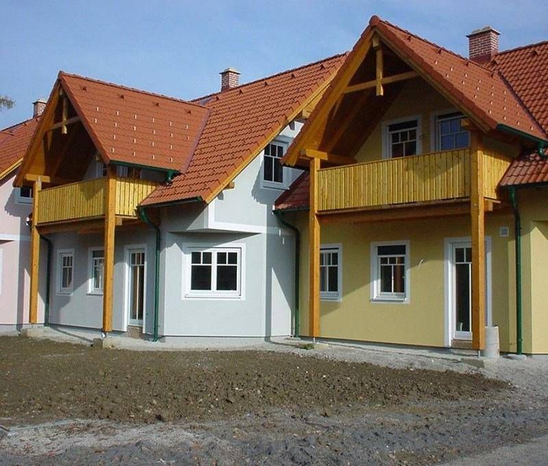 Eine Reihe von Häusern mit roten Dächern und gelben Wänden. Jedes Haus hat einen Balkon und weiße Fenster. Der Boden ist noch nicht fertiggestellt.