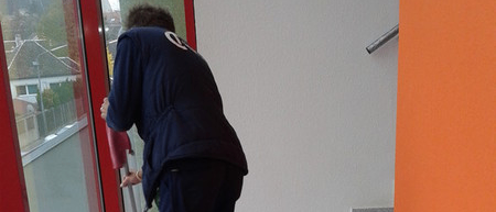 Ein Mann in Uniform reinigt einen Boden neben einer Tür mit einem Mopp.