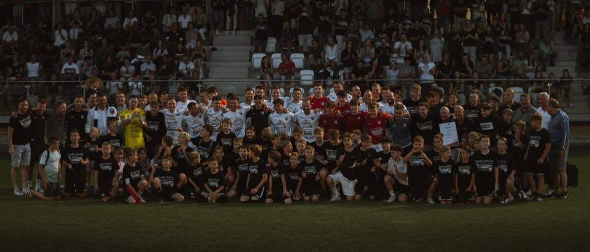 Eine Fußballmannschaft posiert für ein Gruppenfoto auf dem Spielfeld, während eine jubelnde Menge im Hintergrund steht.