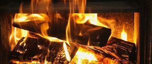 Ein Kamin mit brennenden Holzscheiten, die ein warmes Licht verbreiten. Die Flammen flackern und steigen auf und beleuchten den dunklen Raum.