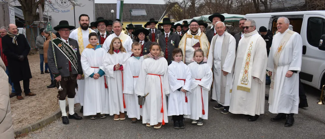 Eine Gruppe von Menschen in weißen Gewändern, einschließlich Kinder, stehen vor einem Gebäude mit Priestern. Sie scheinen für ein Foto zu posieren.