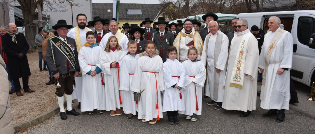 Eine Gruppe von Menschen in weißen Gewändern, einschließlich Kinder, stehen vor einem Gebäude mit Priestern. Sie scheinen für ein Foto zu posieren.
