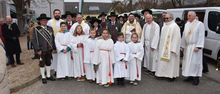 Eine Gruppe von Menschen in weißen Gewändern, einschließlich Kinder, stehen vor einem Gebäude mit Priestern. Sie scheinen für ein Foto zu posieren.