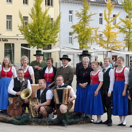 Eine Gruppe von Musikern und Tänzern in traditionellen Kostümen posiert für ein Foto vor einem Gebäude mit Herbstbäumen.