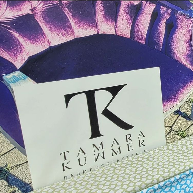 Ein violetter Samtsofa mit einem Schild davor, auf dem Tamara Kummer Raumausstatterin steht. Ein Hund liegt in der Nähe auf dem Boden.