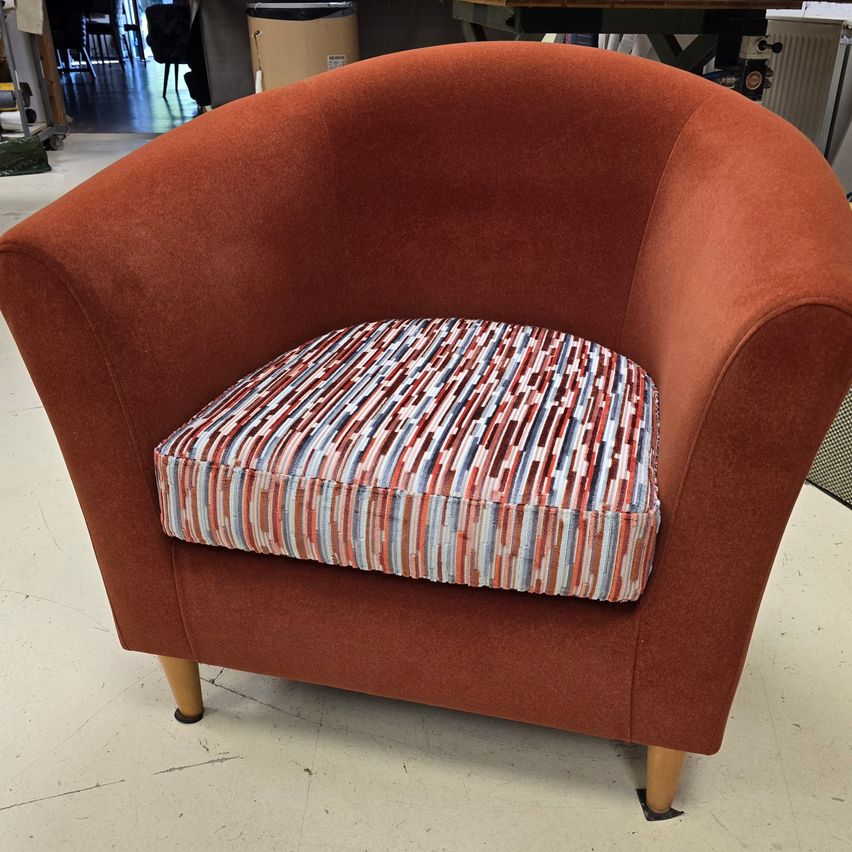 Ein runder, brauner Sessel mit gemusterter Sitzauflage steht in einer Werkstatt. Der Stuhl hat Holzbeine und eine samtartige Textur.