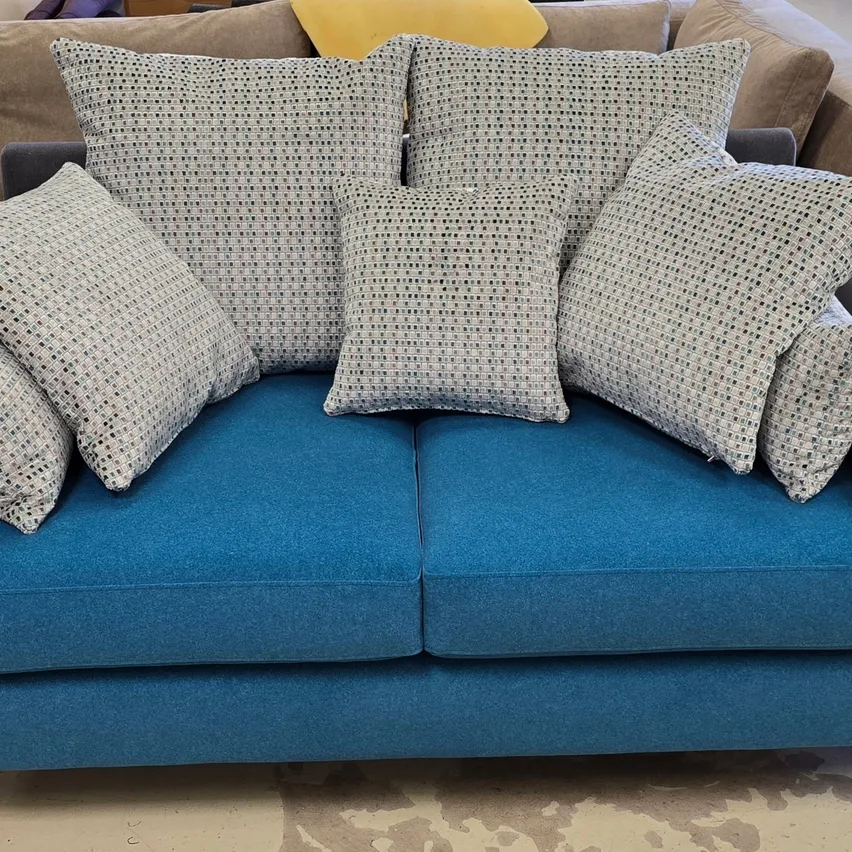Ein blaues Sofa mit mehreren dekorativen Kissen, einschließlich einem gelben, auf einem Holzboden.