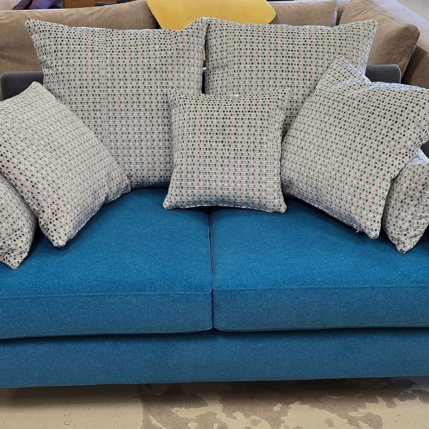 Ein blaues Sofa mit mehreren dekorativen Kissen, einschließlich einem gelben, auf einem Holzboden.