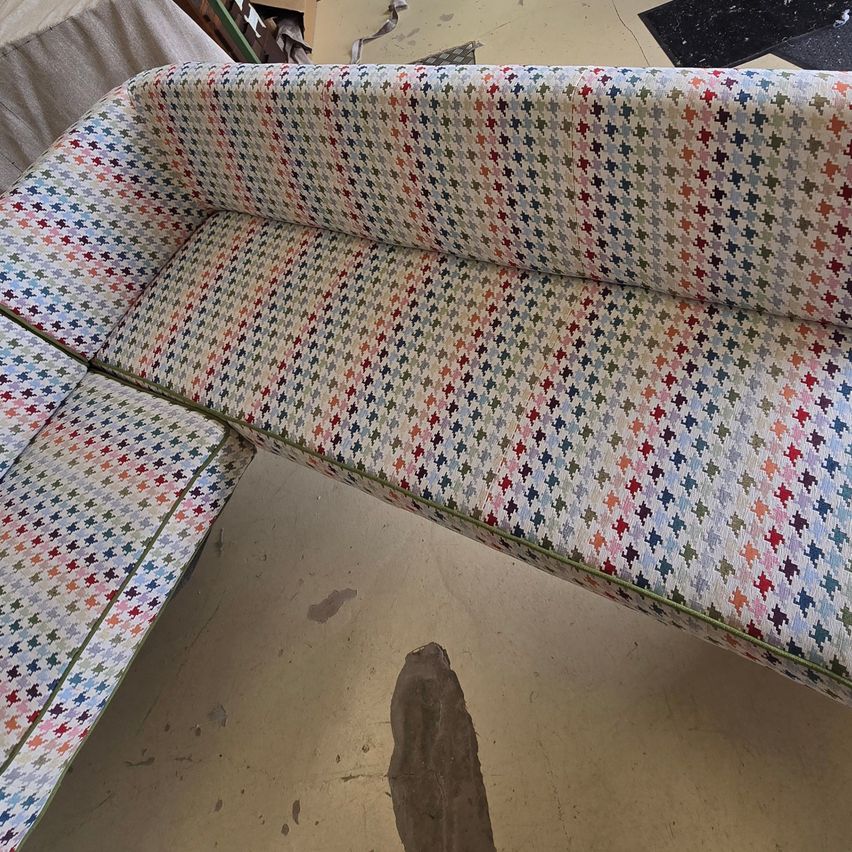 Ein mehrfarbiges Sofa mit geometrischem Muster auf der Polsterung, auf einem Boden platziert. Das Sofa hat ein L-förmiges Design.